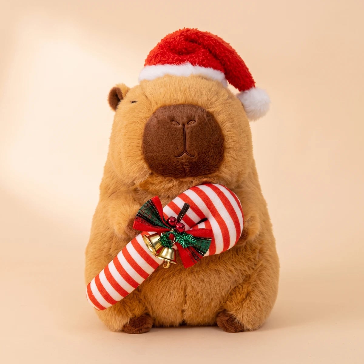 Front view of the Christmas capybara plush with a Santa hat hugging a candy cane with jingle bells