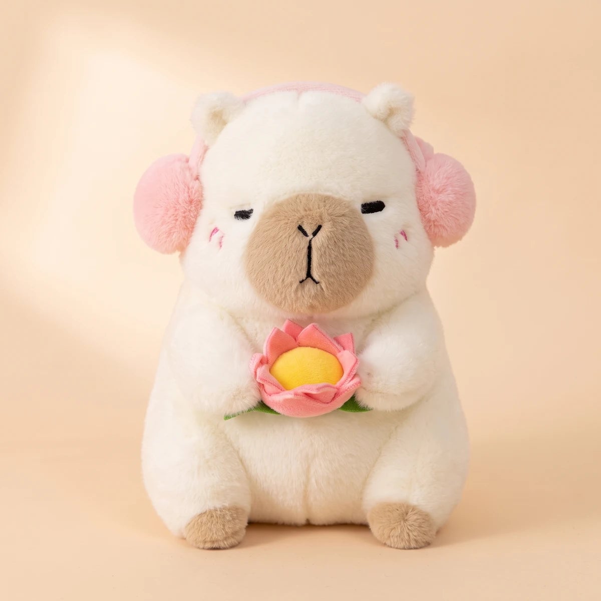 Front view of the white capybara plush with pink headphones holding a pink lotus flower