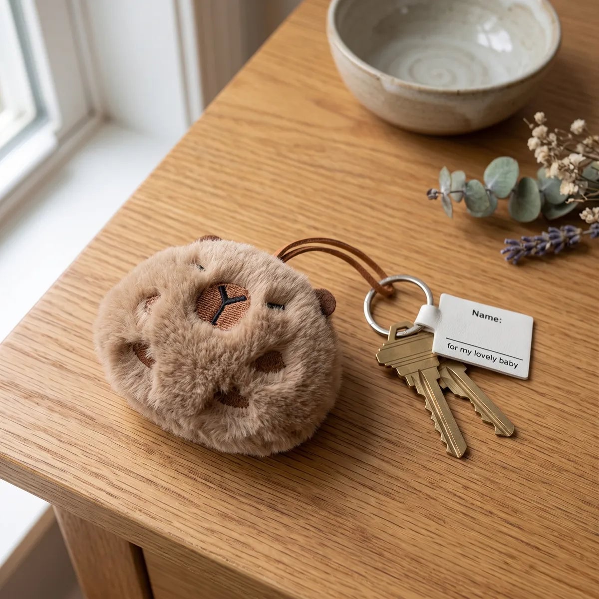 Ball capybara keychain on a wooden table beside a set of house keys