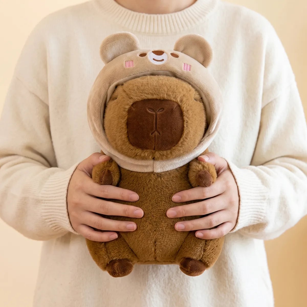 Person hugging the bear capybara plush against a knit sweater