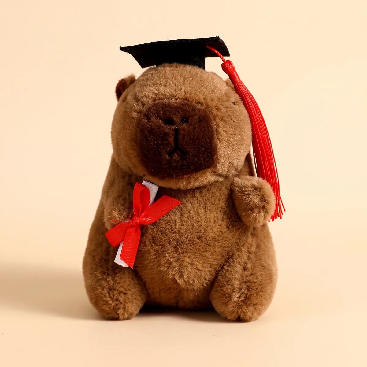 Front view of the cocoa brown graduation capybara plush with a red tassel and diploma