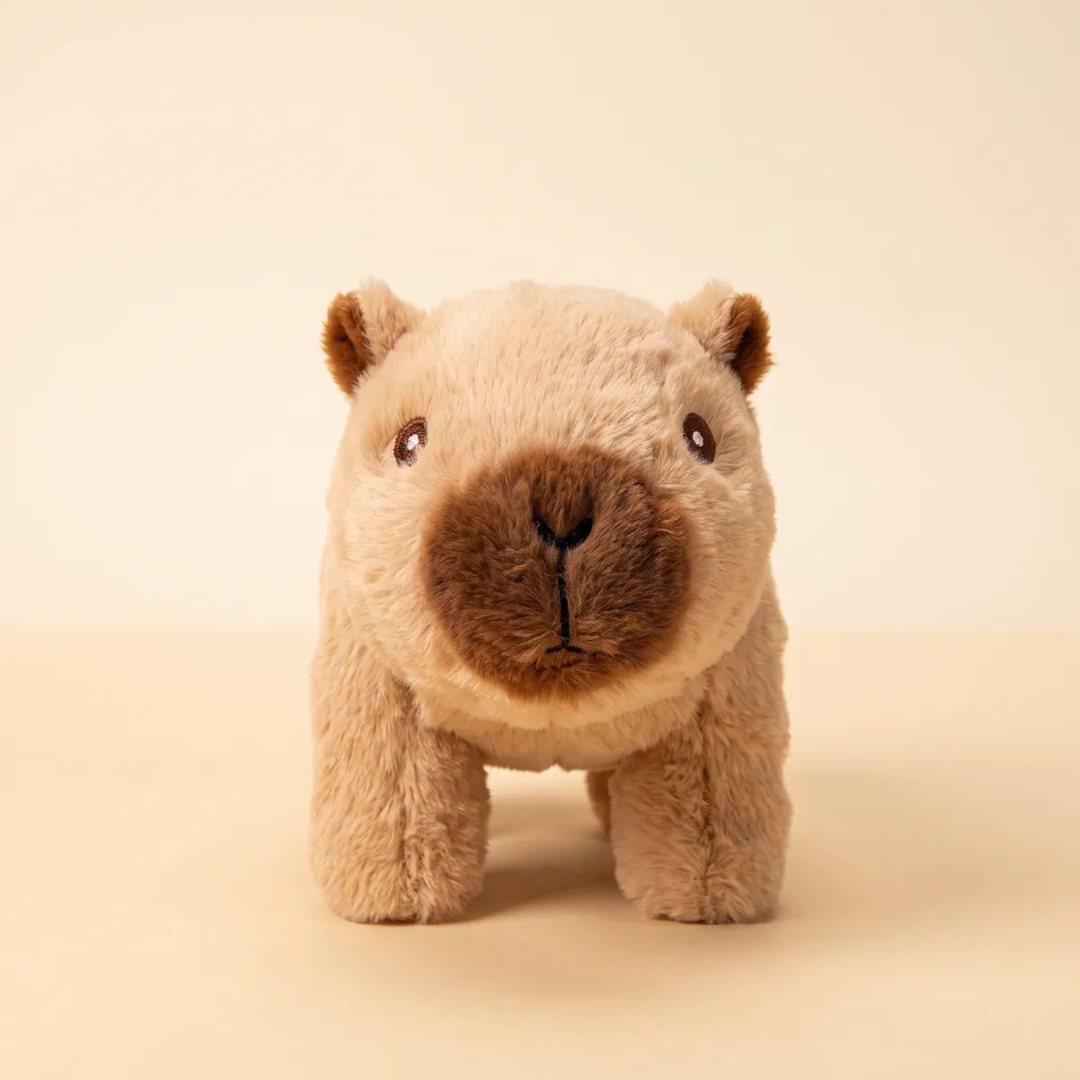 Brown walking capybara toy standing on all four legs in caramel fur, photographed straight on against a cream sweep