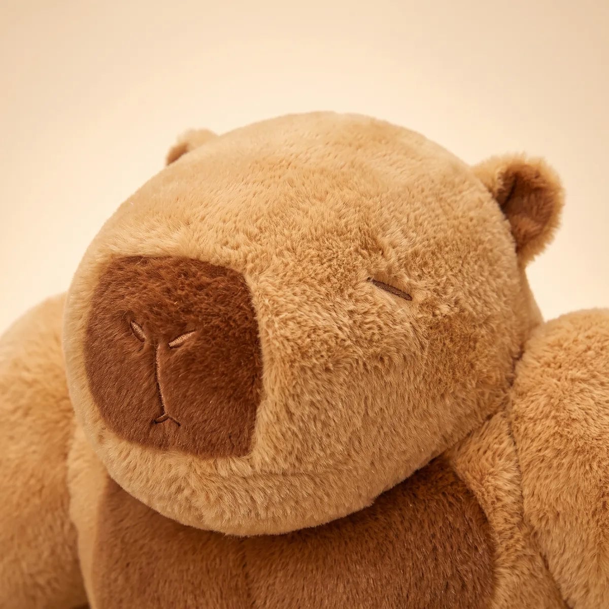 Close up of the embroidered sleeping face and brown muzzle of the buff capybara plush