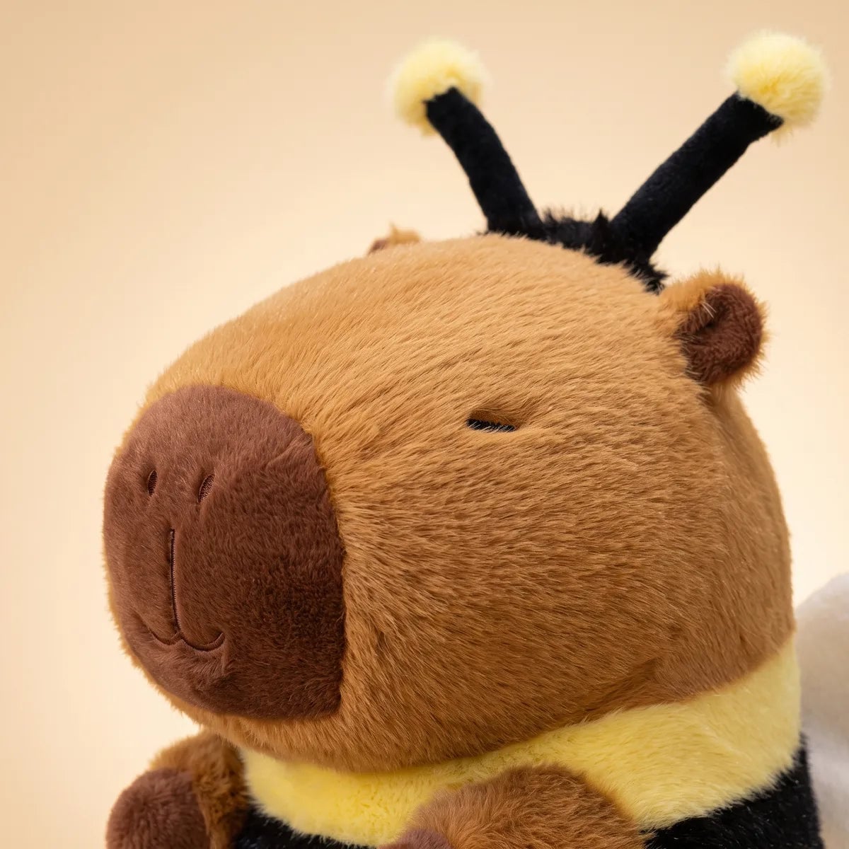 Close up of the capybara bee plush head showing the dark brown muzzle, embroidered eyes and black antennae