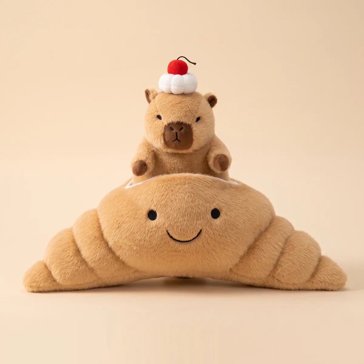 Front view of the capybara croissant plush, the cream topped capybara seated in the smiling tan pastry