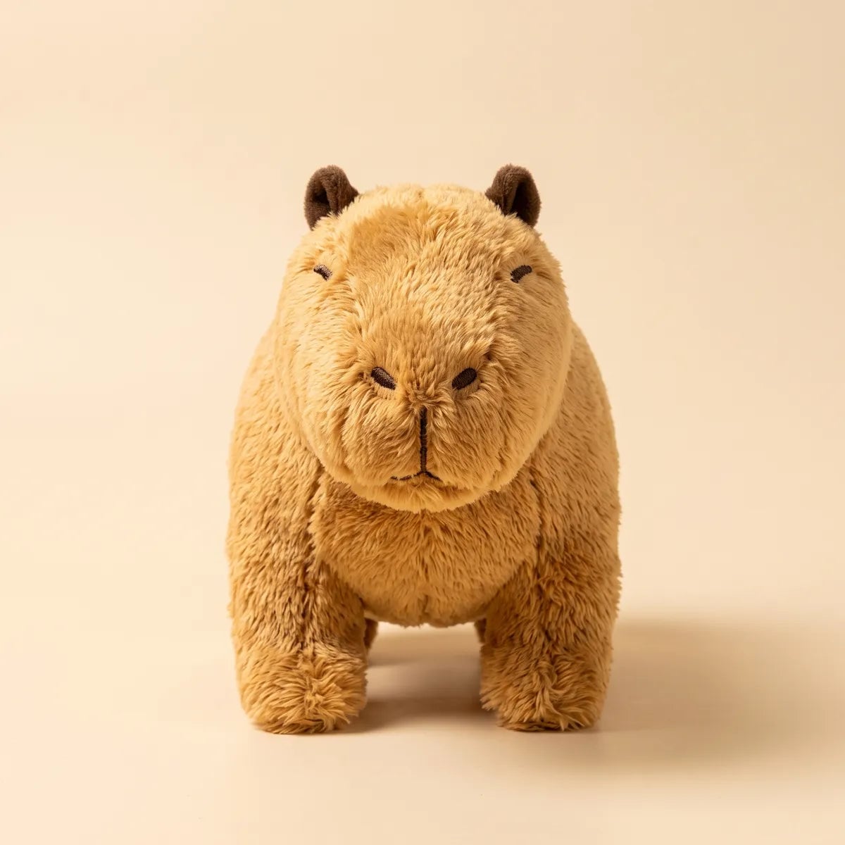 Capybara teddy bear plush photographed head on, standing squarely on all four legs against a cream backdrop.