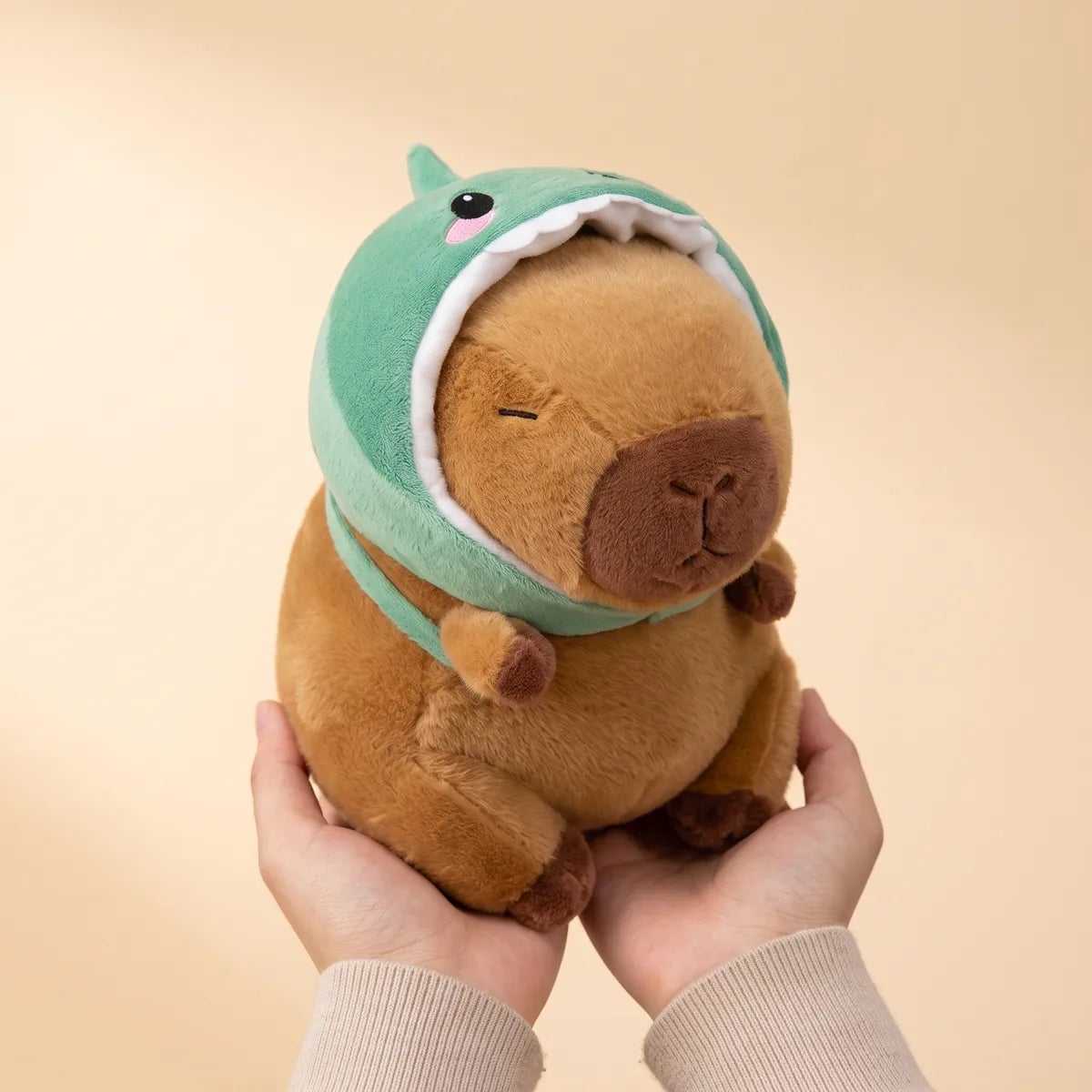 Hands cradling the dino capybara plush to show its real size