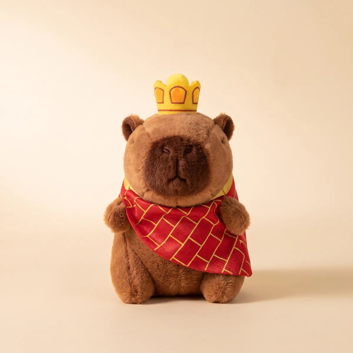 Front view of the 5 in king mini capybara plush wearing its yellow crown and red lattice cape