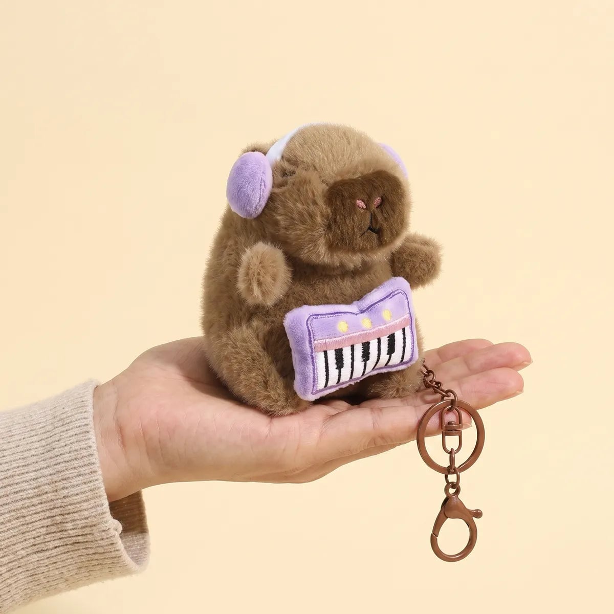 Piano capybara keychain resting in a palm with the bronze chain and lobster clasp hanging below