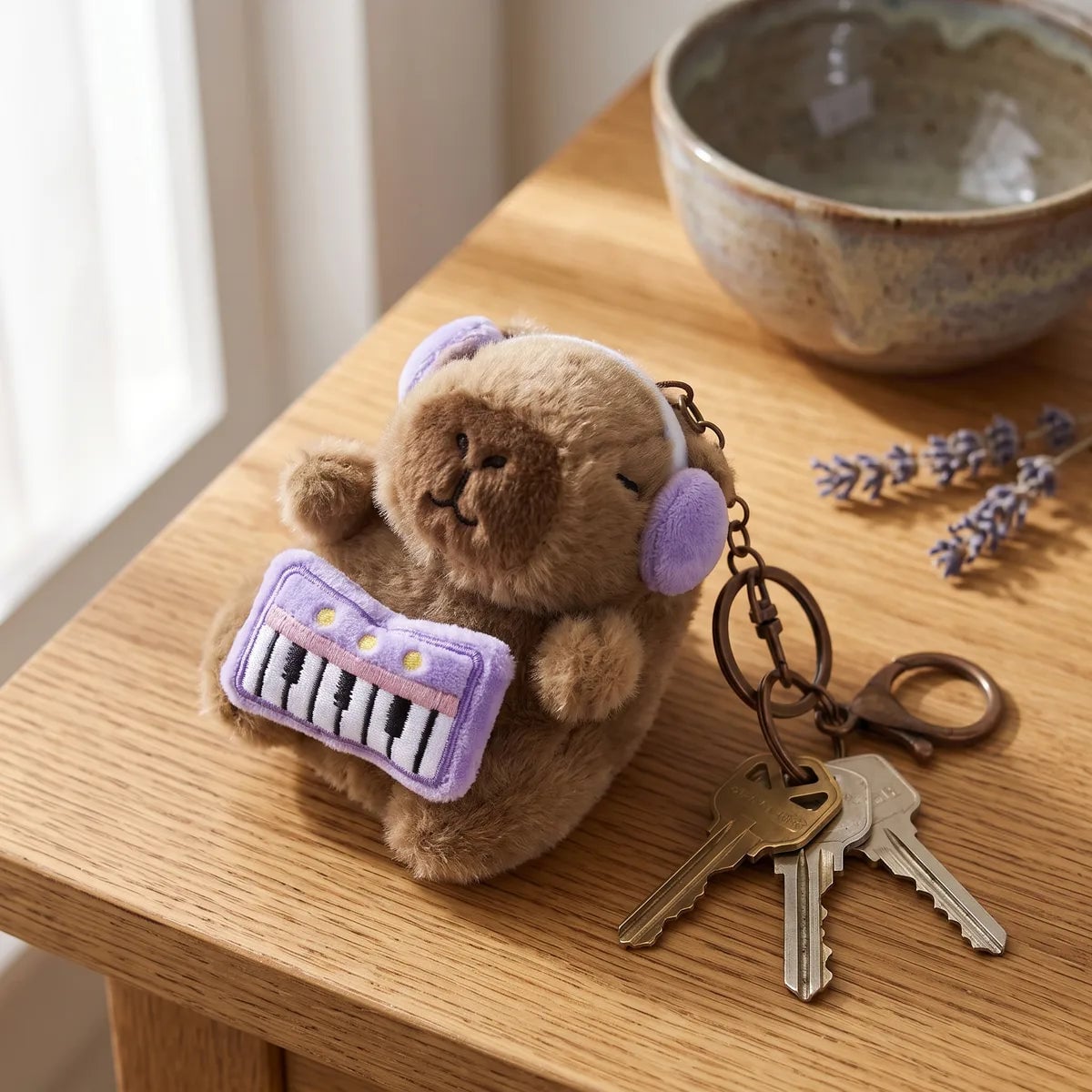 Piano capybara keychain on a wooden table attached to a set of house keys beside dried lavender
