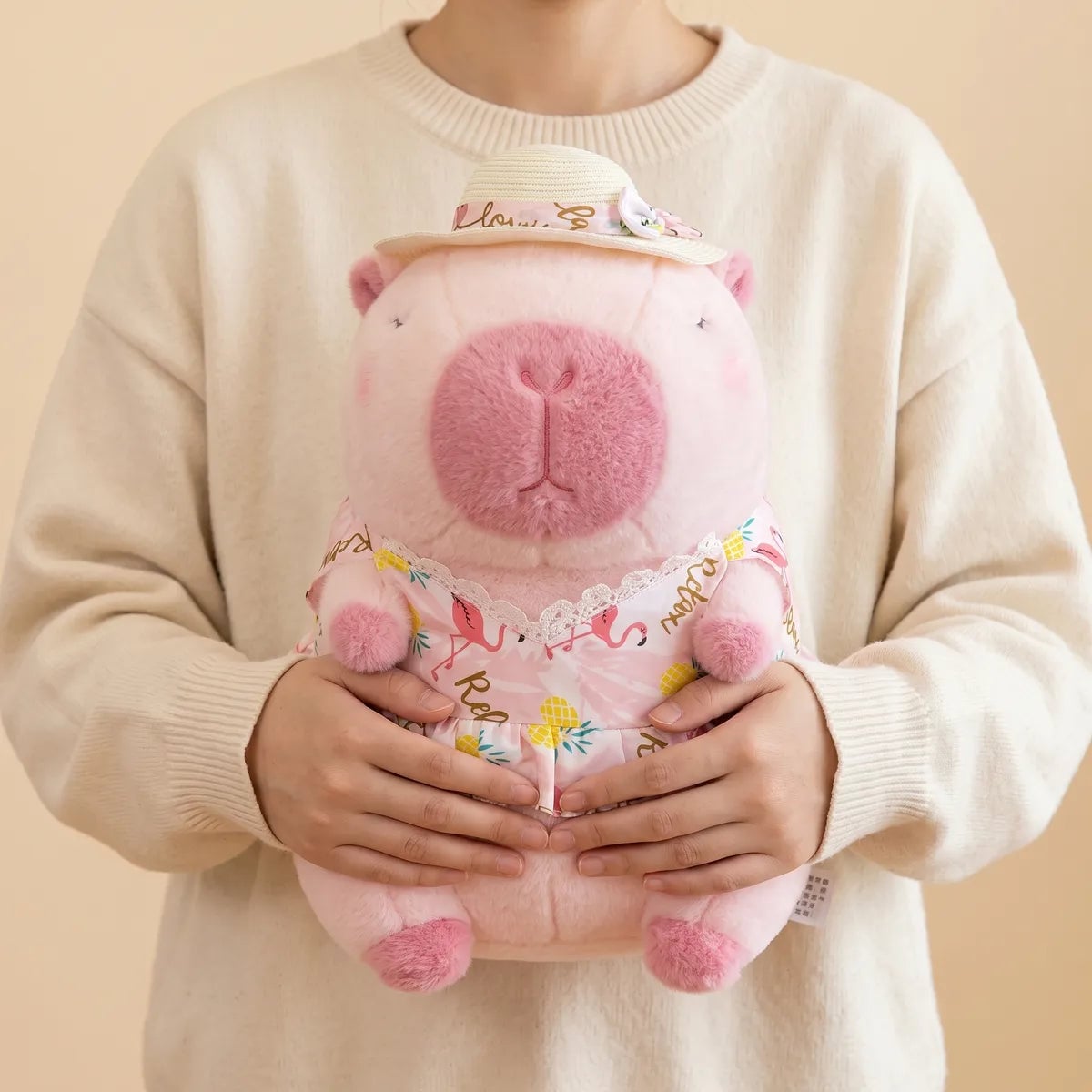 Person in a cream sweater holding the pink capybara plush against their chest with both hands