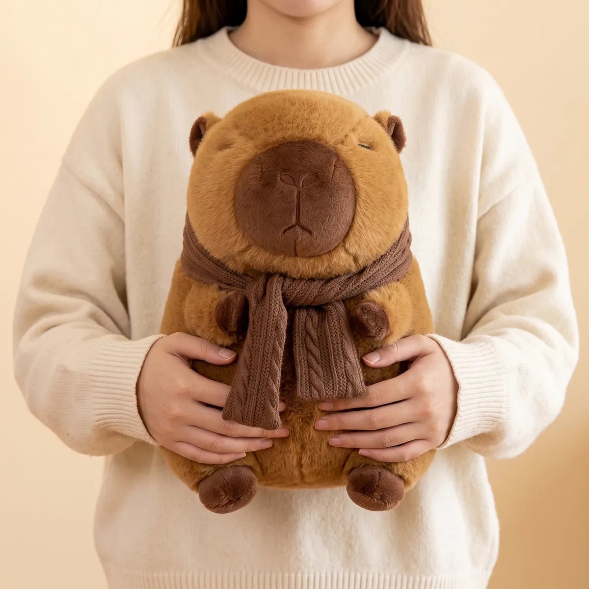 Scarf capybara plush carried against a cream sweater with the scarf tail hanging down