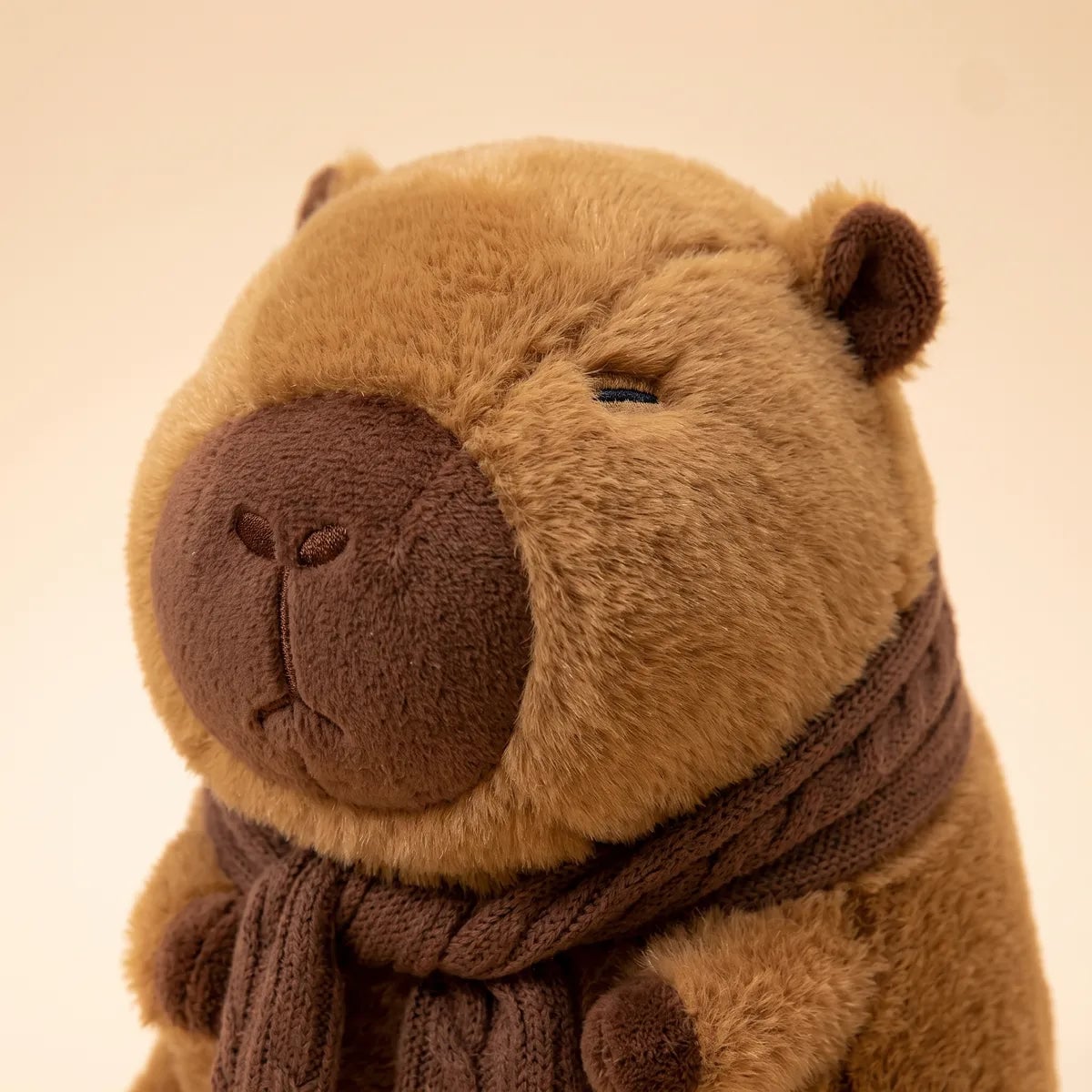 Close up of the scarf capybara plush face with a dark chocolate muzzle