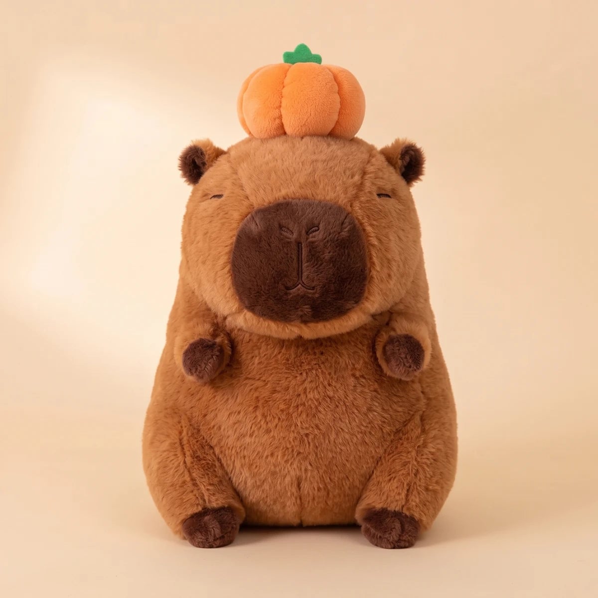 Front view of the capybara with pumpkin on head plush on a peach studio backdrop
