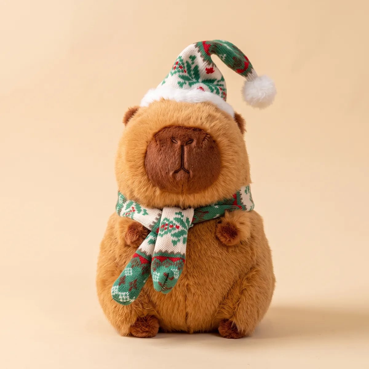 Front view of the Christmas capybara plush with a green and white knit hat and scarf patterned with red berries