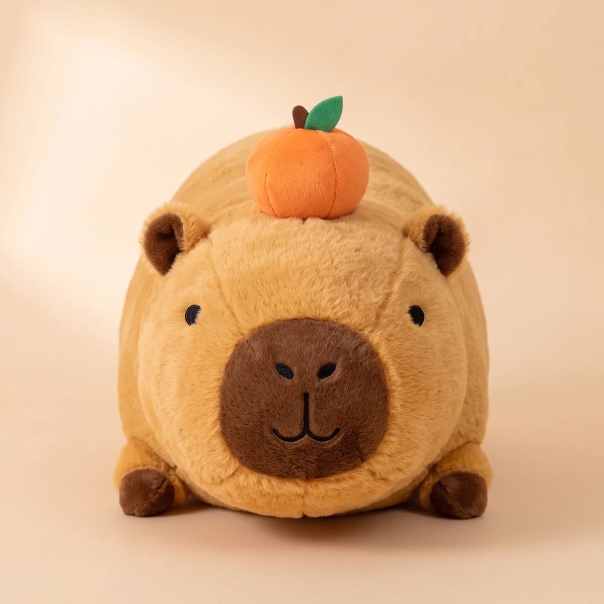 Front view of the lying capybara plush with an orange on its head