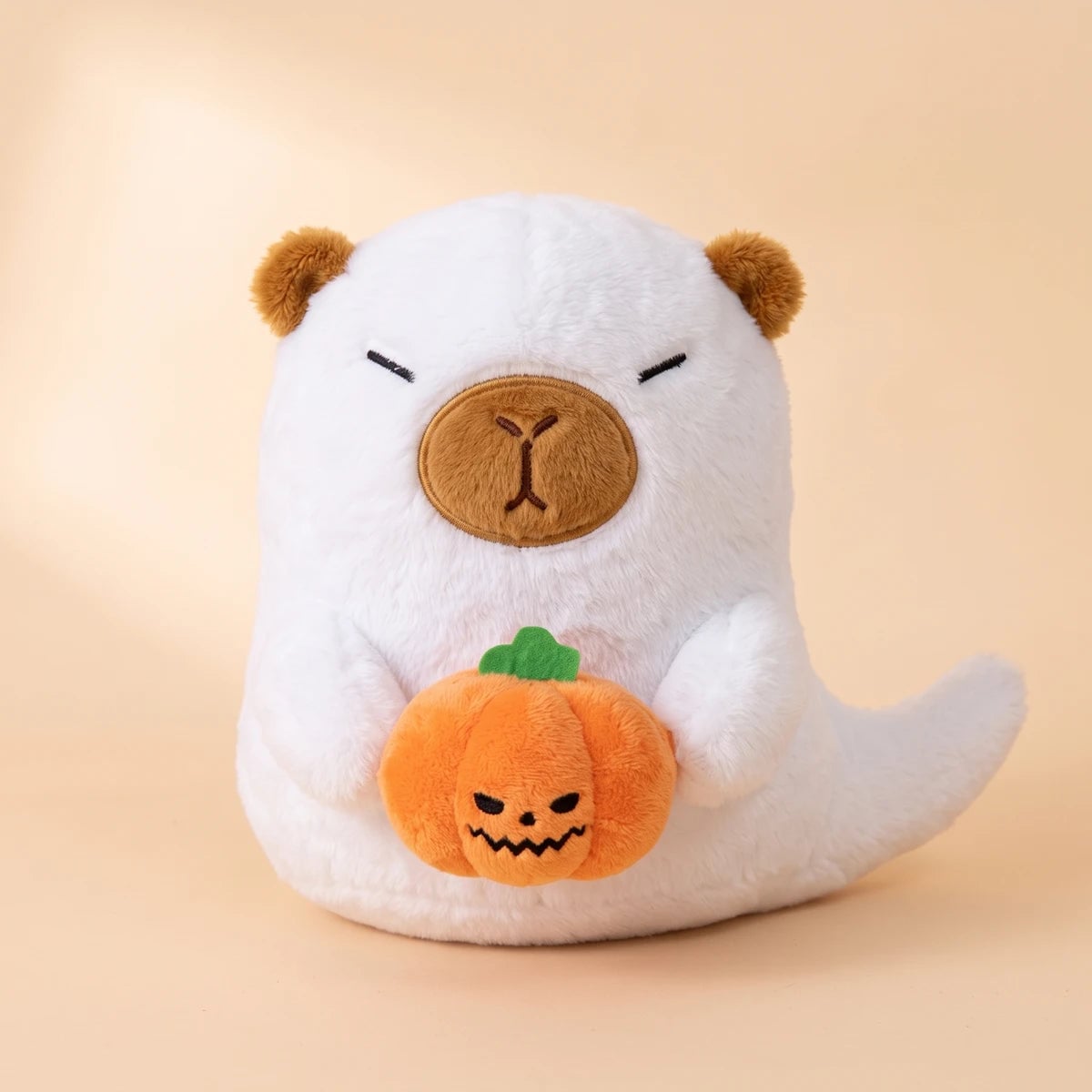 Front view of the white ghost capybara plush with its orange pumpkin