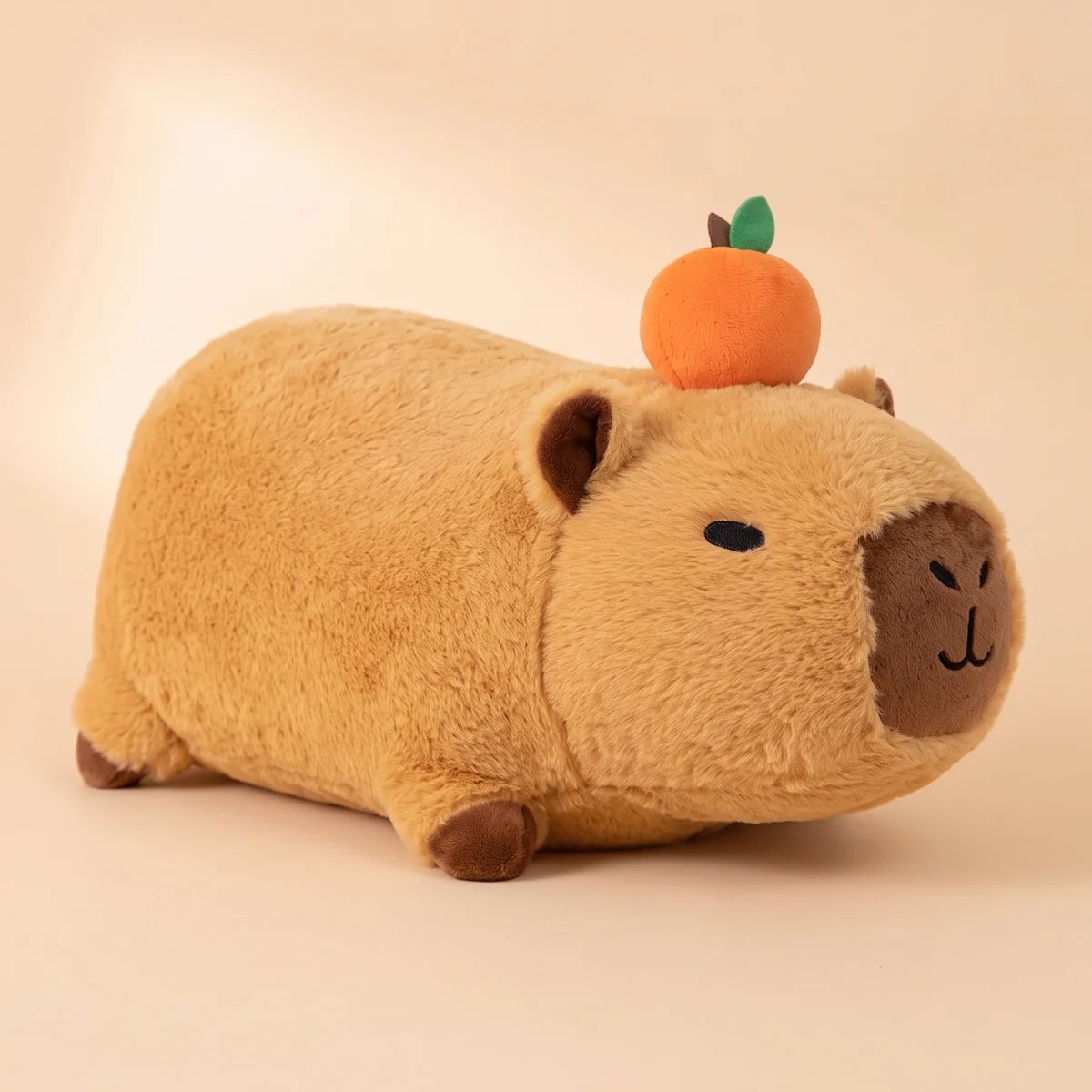 Side view of the lying capybara plush with an orange on its head