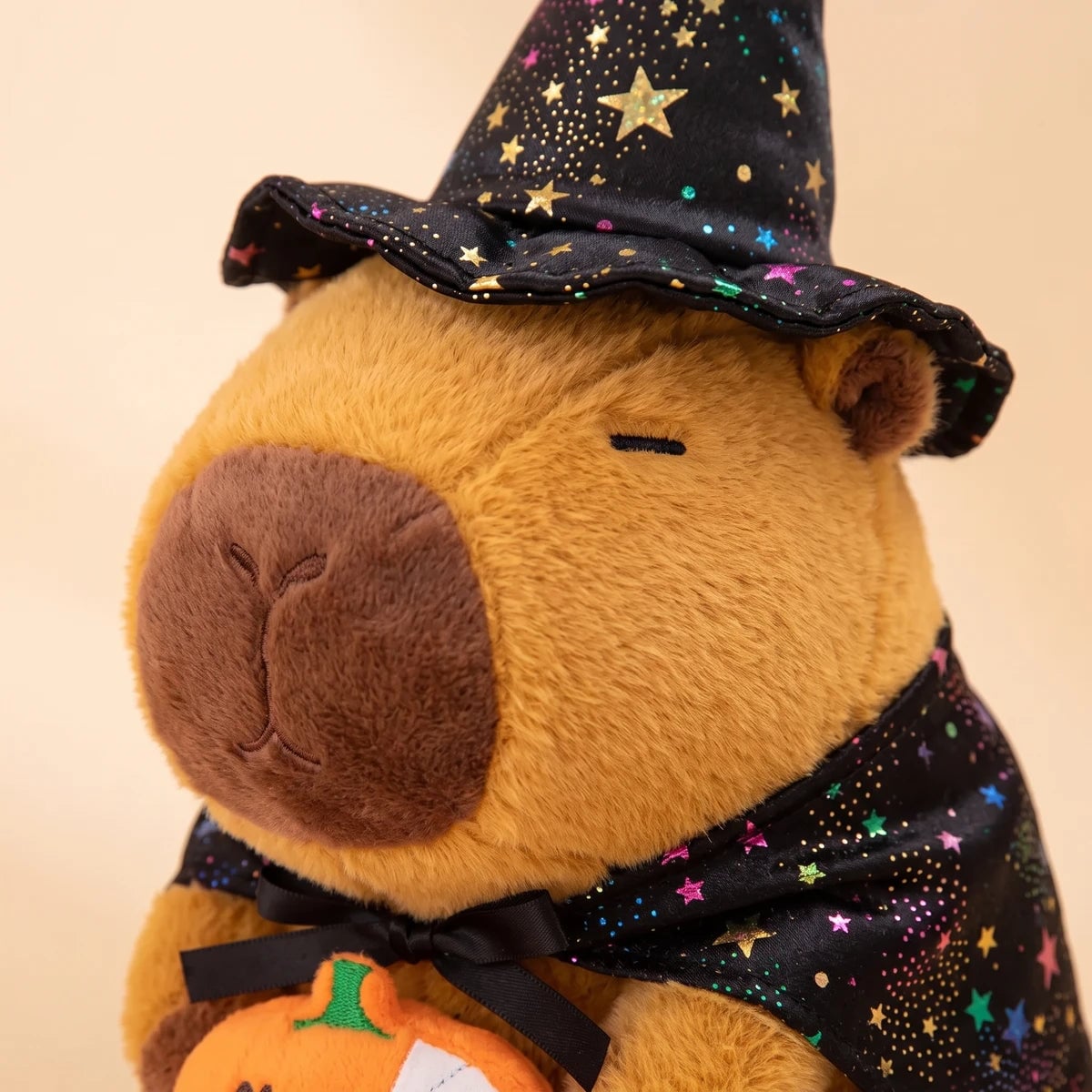Close-up of the face of the pumpkin witch capybara plush under its starry witch hat