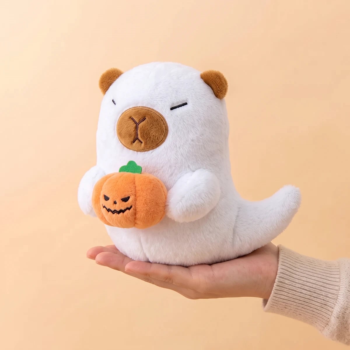 White ghost capybara plush resting on an open hand to show its 7 in size