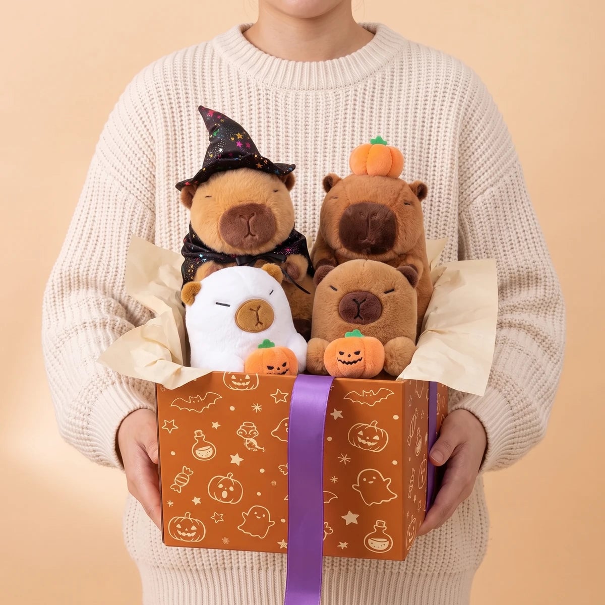 Person in a cream sweater holding the four Halloween capybara plush