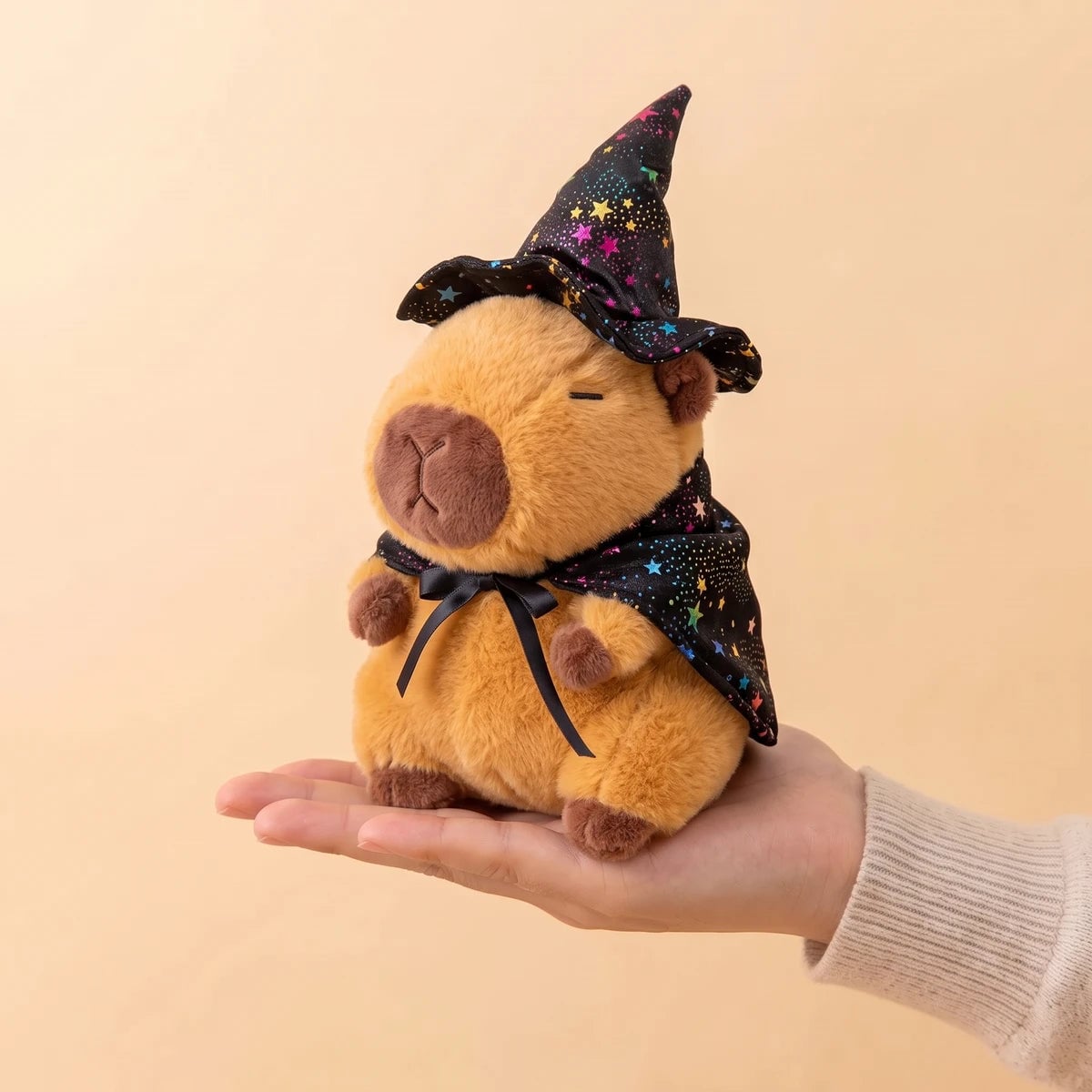 Witch capybara plush with a starry black hat and cape sitting on an open hand