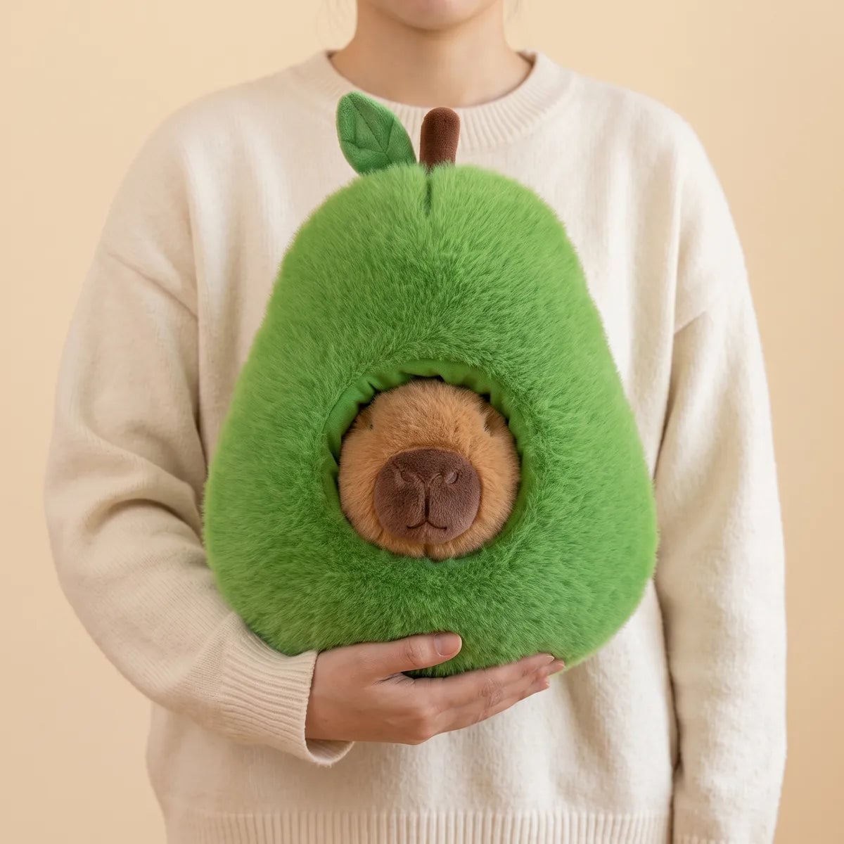 Person holding the green avocado house from the capybara plush set against the chest with both arms
