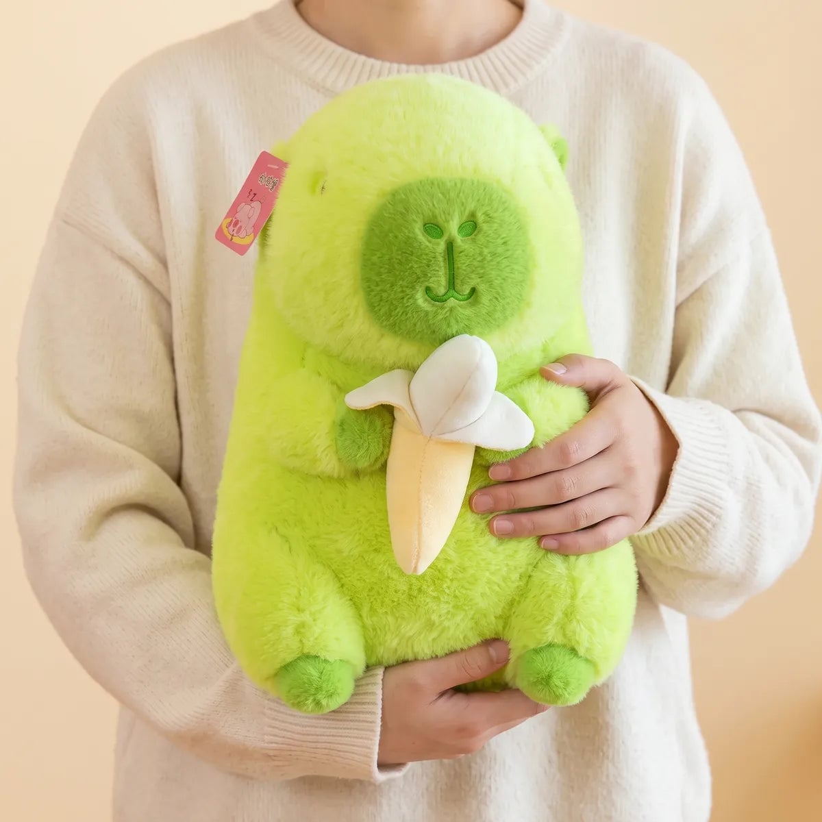 Banana capybara plush carried in both arms against a cream sweater