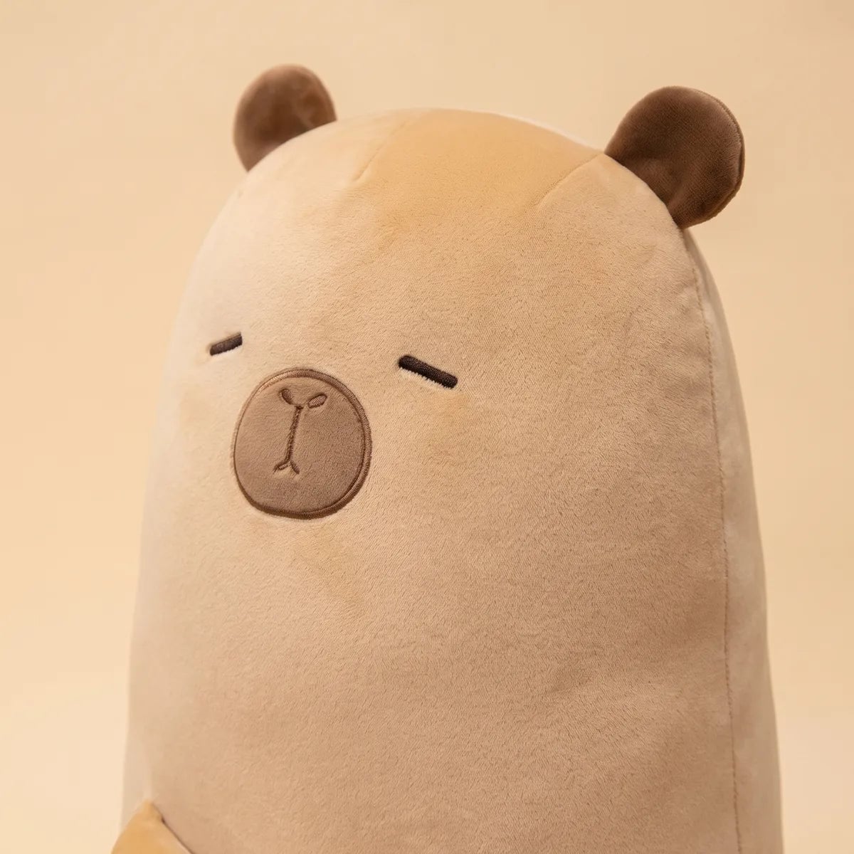 Close up of the big capybara stuffed animal plush face showing brown ears, stitched eyes and the embroidered muzzle patch.