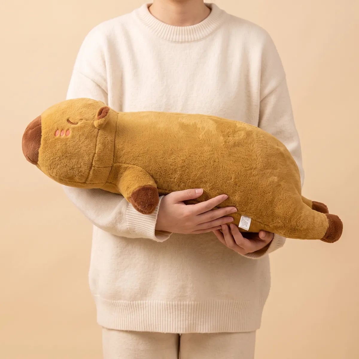 Person holding the brown pillow giant capybara plush to show its length