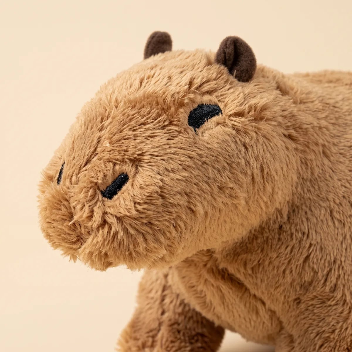 Close up of the capybara teddy bear plush face with black satin stitched eyes, stitched nostrils and small dark ears.