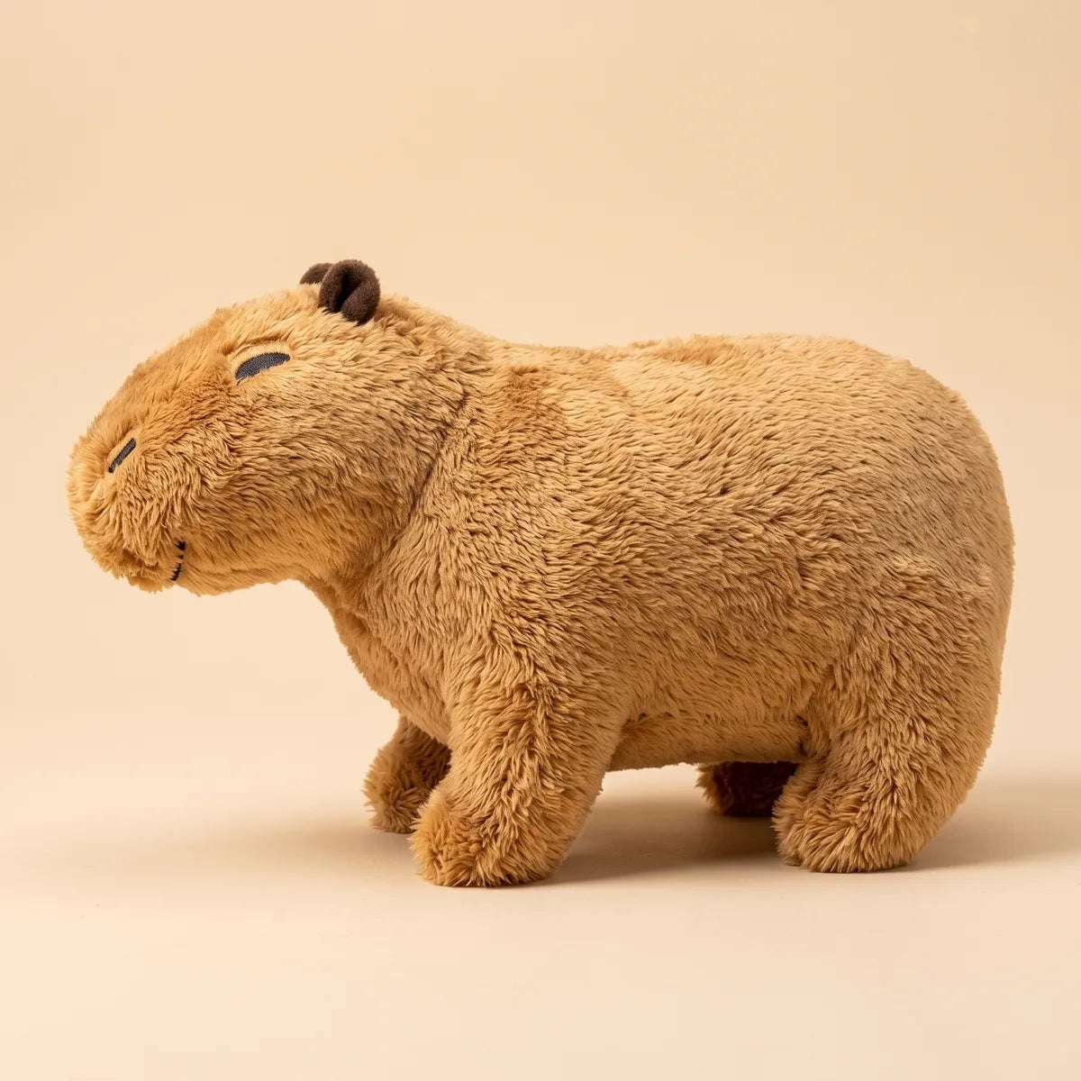 Side profile of the capybara teddy bear plush showing its long barrel body and shaggy honey brown fur.