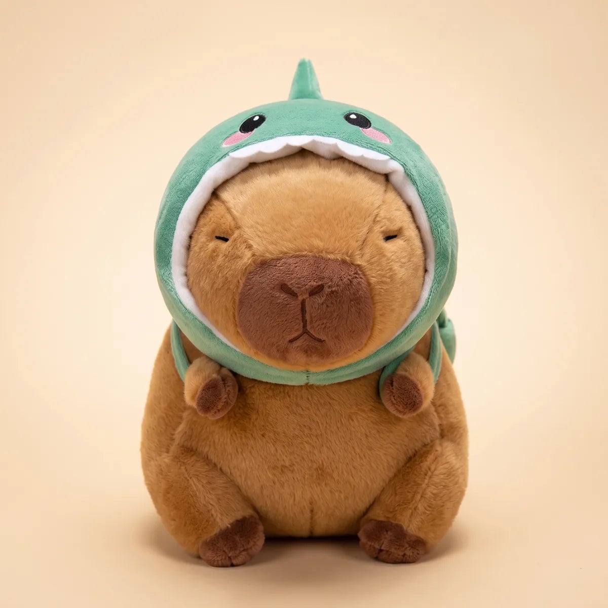 Brown dino capybara plush seen from the front in its green dinosaur hood