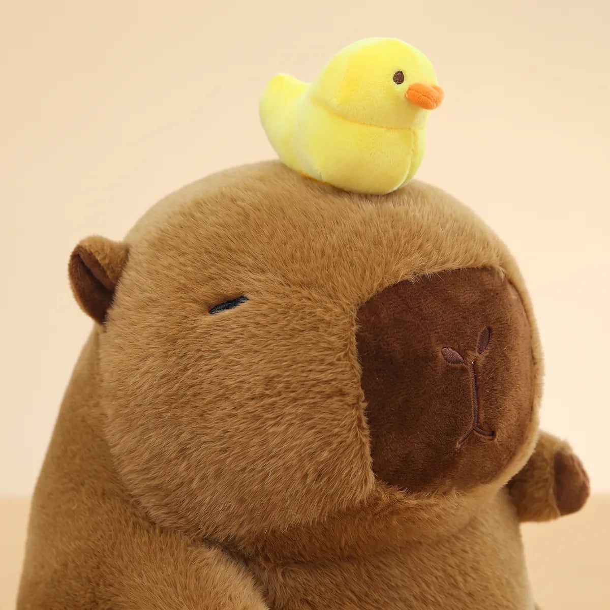Close-up of the capybara with duck on head plush showing the bright lemon duckling and its orange bill above the chocolate muzzle patch