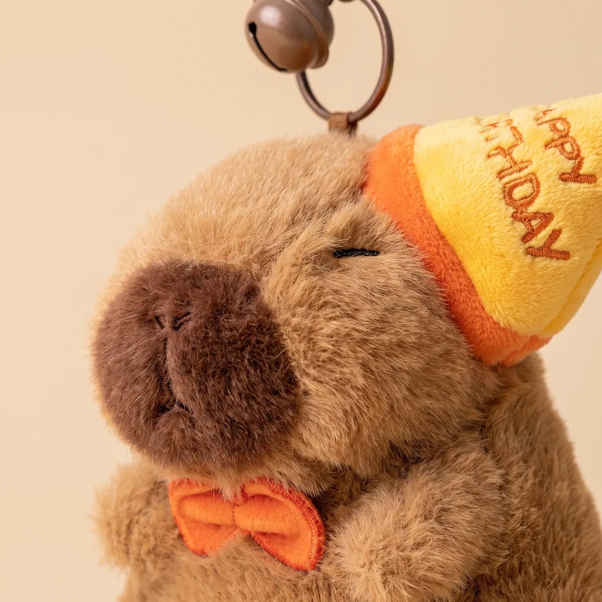 Close-up of the capybara keychain wearing a yellow HAPPY BIRTHDAY cone hat and an orange bow tie