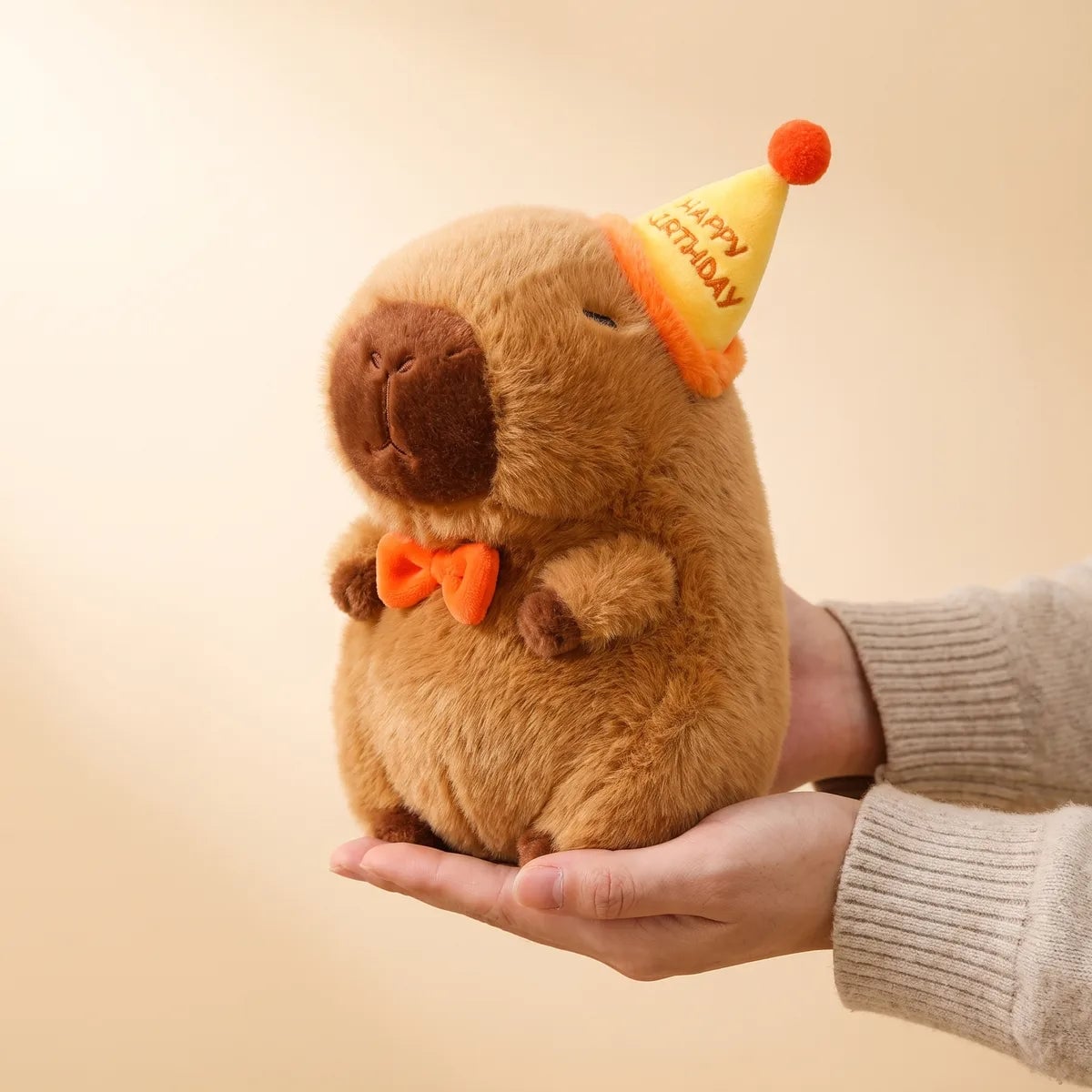 Happy birthday capybara plush cradled in one hand and seen from the side