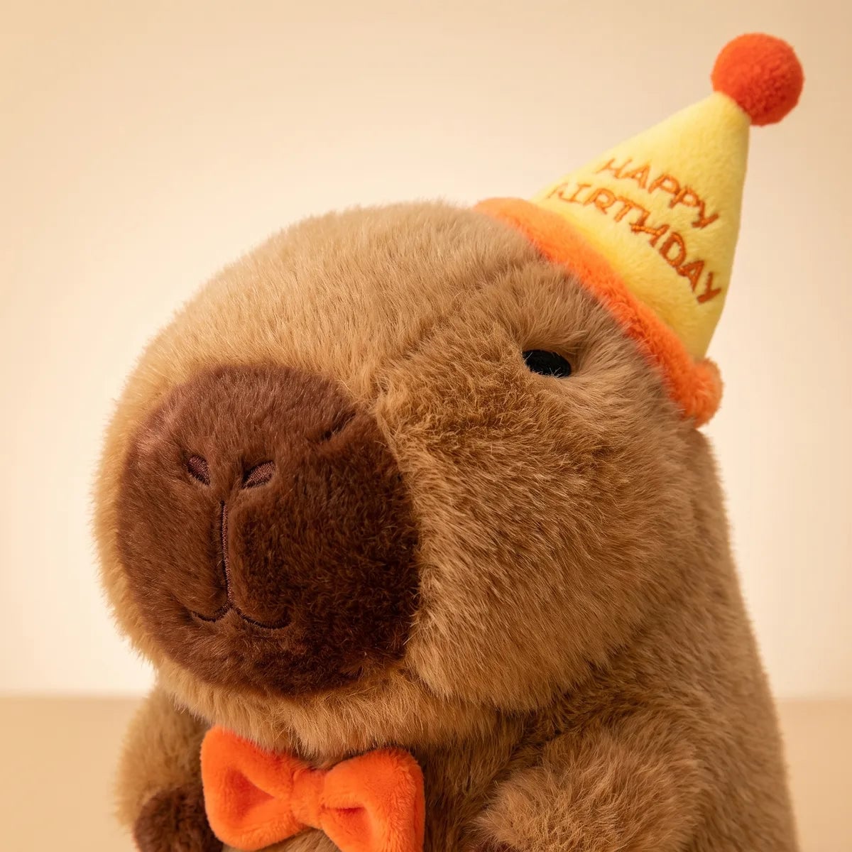 Close-up of the happy birthday capybara plush face with a chocolate snout under its yellow HAPPY BIRTHDAY hat