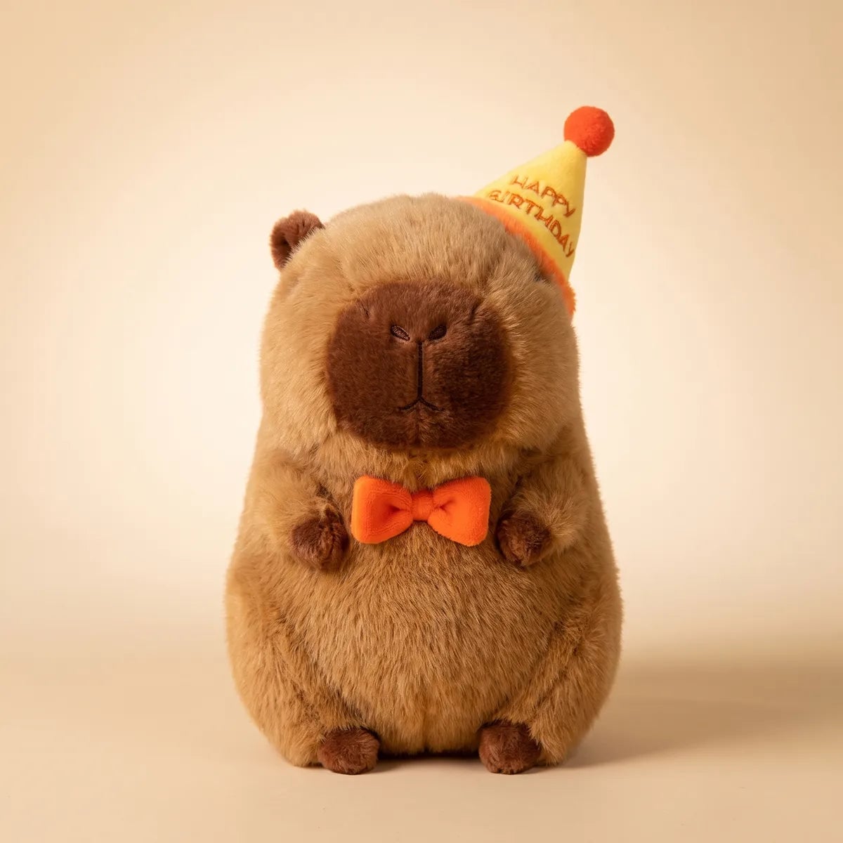 Front view of the 13 in happy birthday capybara plush in its yellow party hat and orange bow tie