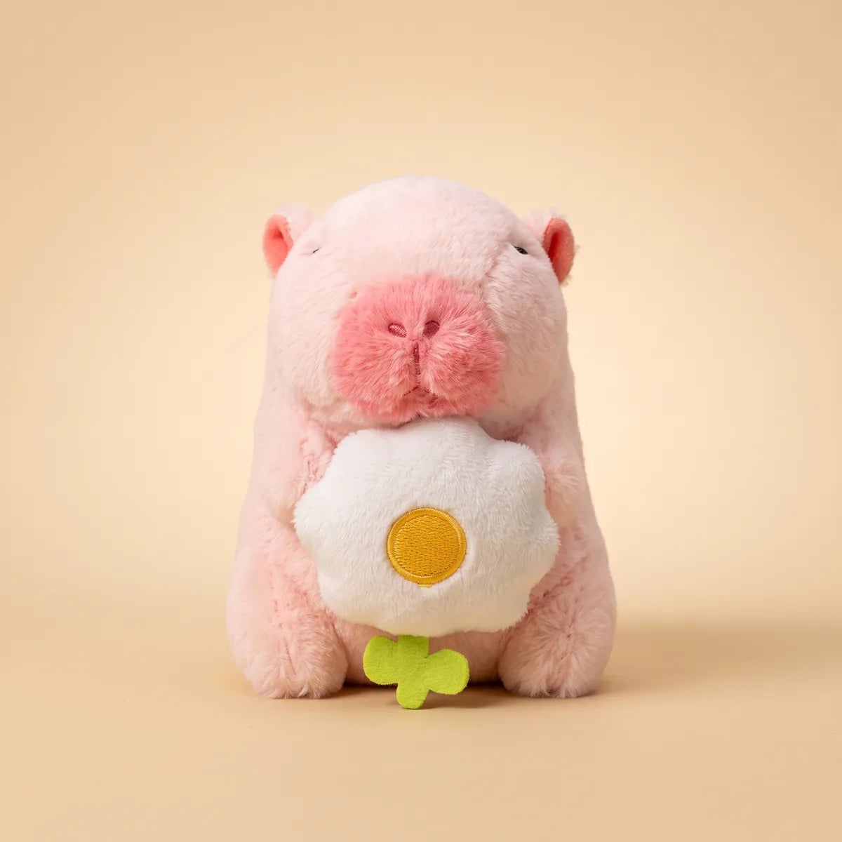 Front view of the pink mini capybara plush hugging a white five petal flower with a yellow center