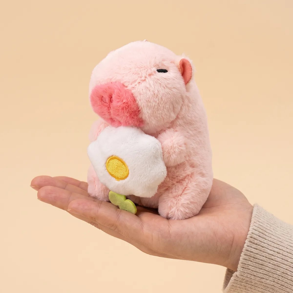 Pink mini capybara plush and its white flower resting on an open palm to show the 4 in size