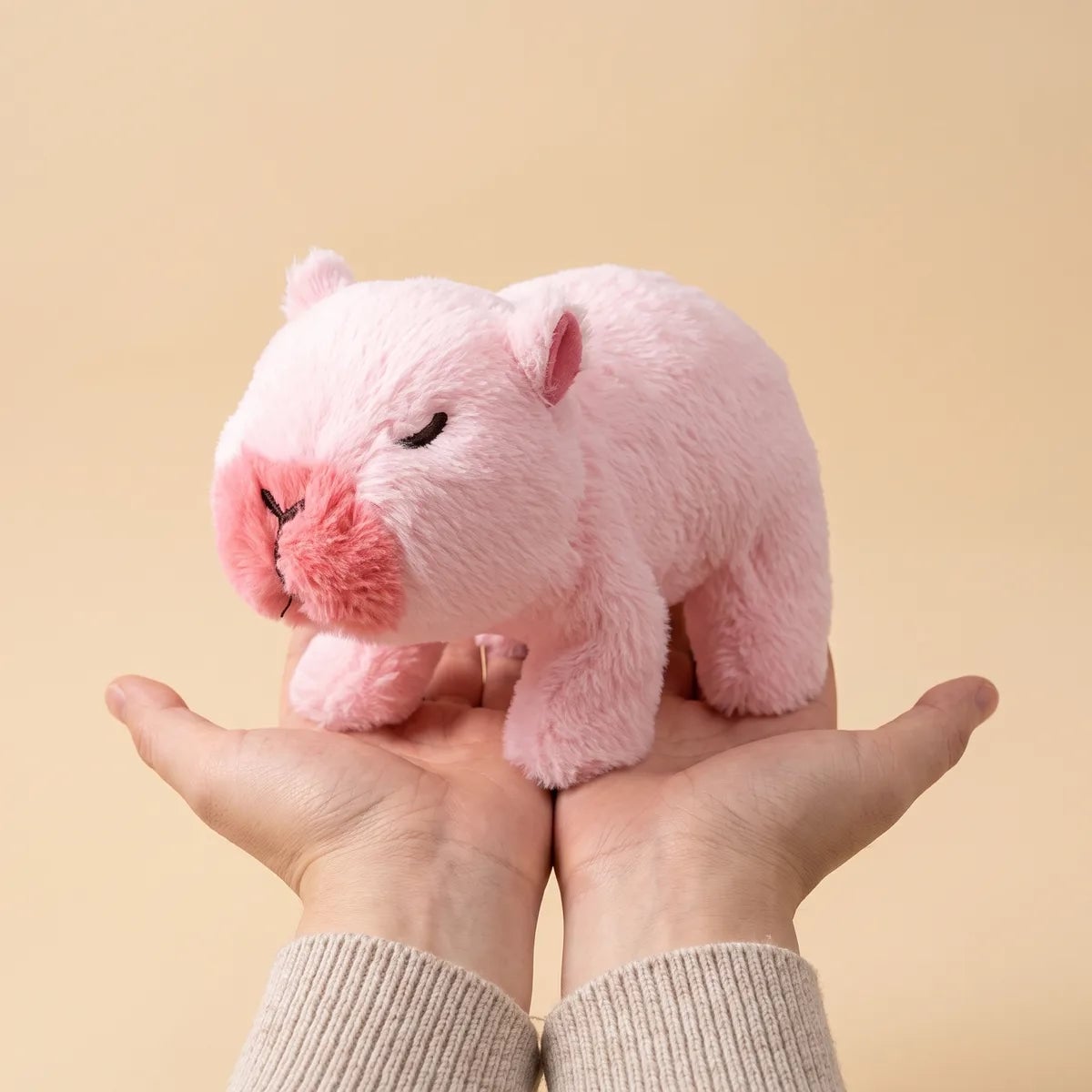 Pink walking capybara toy held in two cupped hands to show the 9 in body length