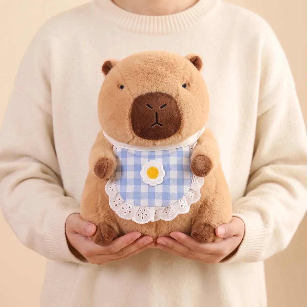 Person holding the capybara plush with its daisy bib against a cream knit sweater