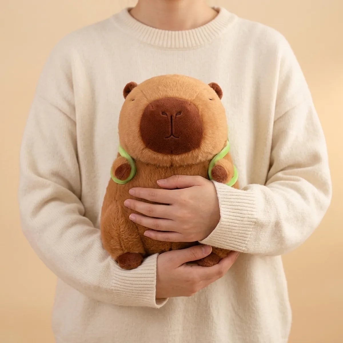 Person holding the turtle backpack capybara plush against a sweater