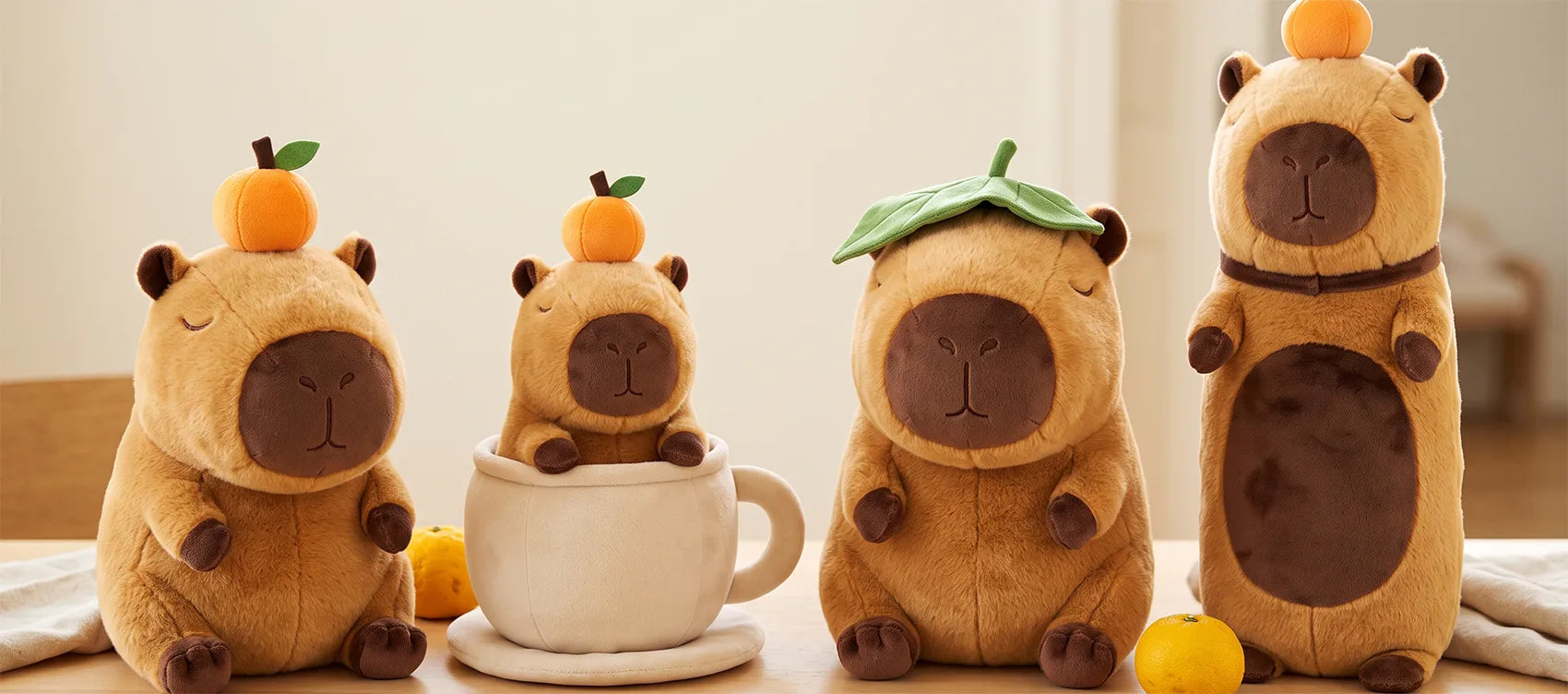 Four capybara plush with fruit and leaf toppers: orange on head, coffee cup capybara, leaf hat capybara and body pillow