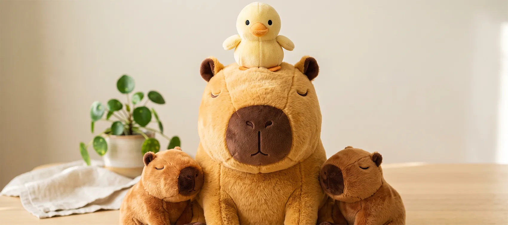 Capybara plush with a yellow duckling perched on its head, flanked by two smaller capybara plush