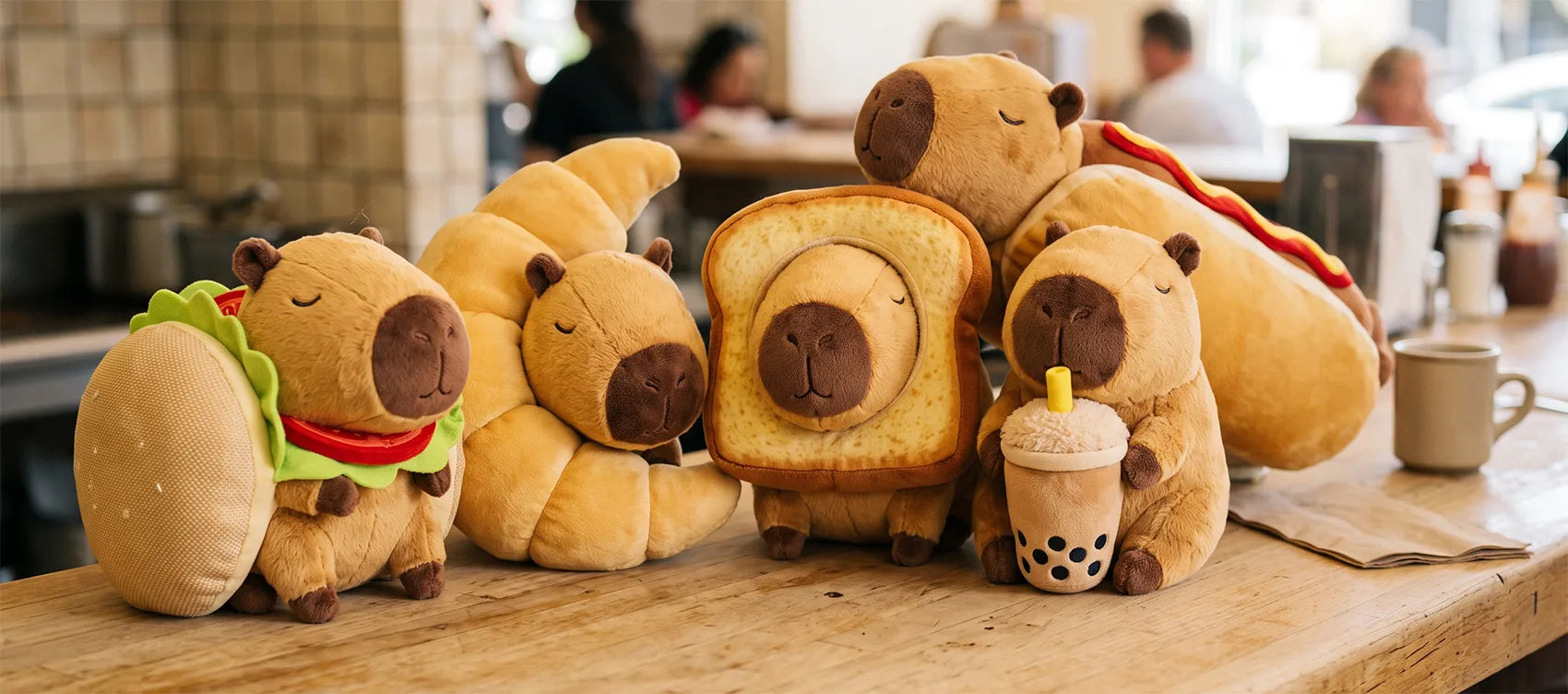 Five food capybara plush on a cafe counter: burger, croissant, toast, boba tea and hot dog